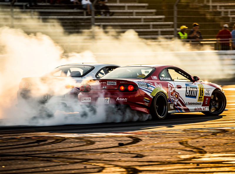 Two drift cars tandem drifting side by side with tire smoke