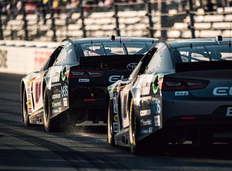 Stock car drafting closely behind another on an oval track