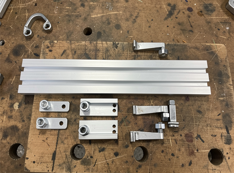 Cut lengths of 8020 aluminum T-slot profile with T-nuts and corner brackets laid out for a sim rig build