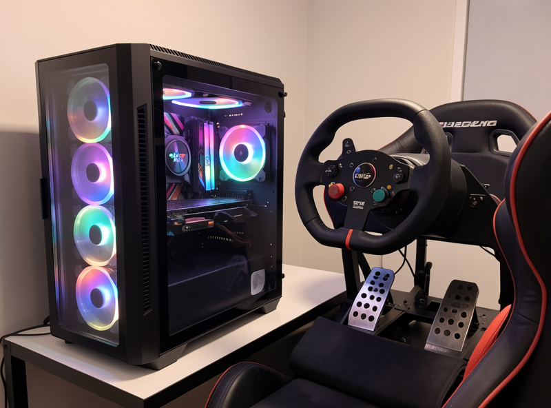 A completed budget sim racing PC next to a wheel and pedals on a cockpit