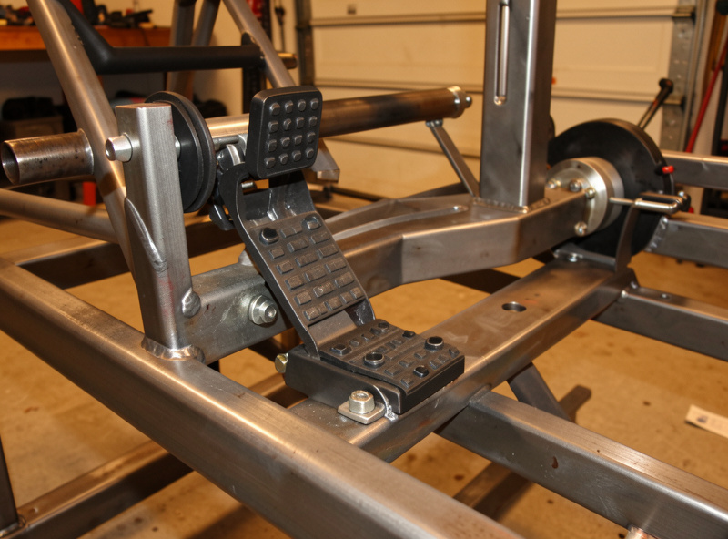 Close-up of a load-cell brake pedal and direct-drive wheelbase on a welded steel sim racing rig