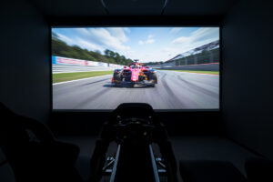 Sim racing cockpit facing a large projected racing image in a dark room