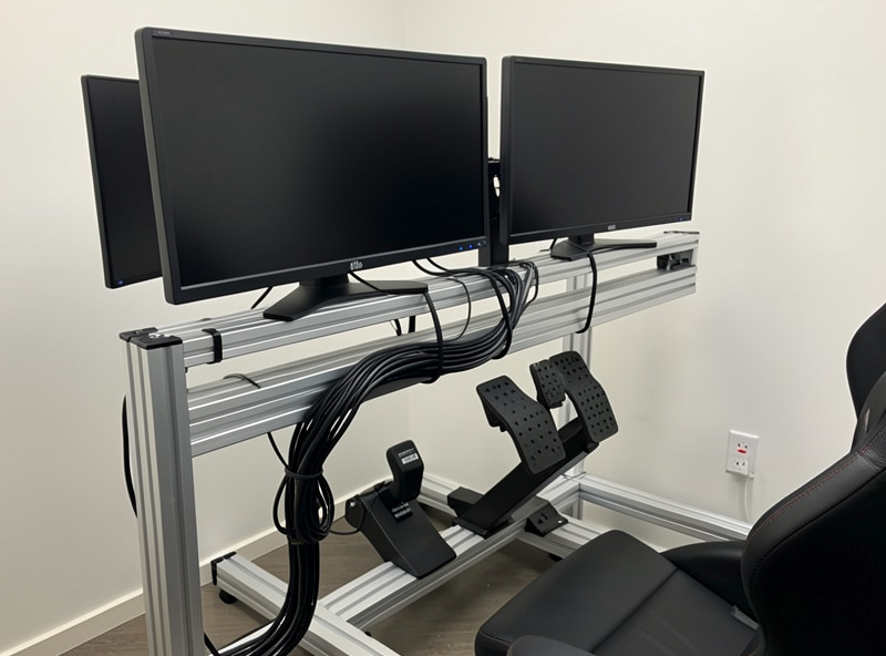 Tidy cable management along an aluminum profile sim rig with monitors mounted and a load-cell pedal set