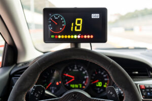 A sim racing dashboard display showing gear, speed and RPM shift lights above a wheel