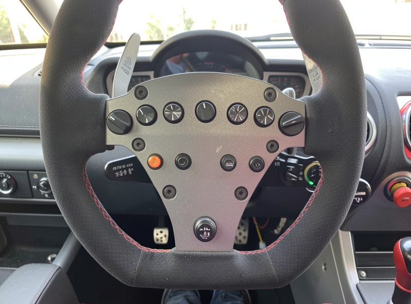 A sim racing wheel rim with a row of rotary dials and a thumb encoder