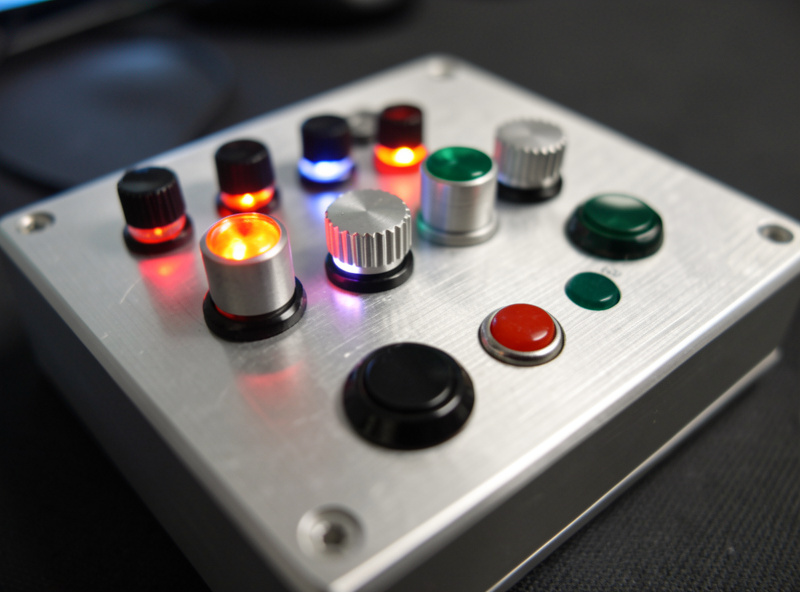 Close-up of an aluminium sim racing button box with backlit toggle switches and rotary encoders