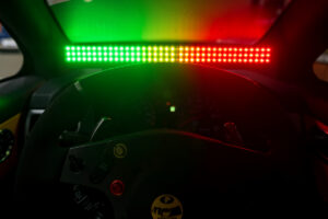 An RPM shift-light LED panel glowing green to red across the top of a sim racing wheel