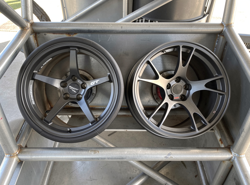 Round formula-style sim racing rim and a sculpted GT rim side by side on a welded steel cockpit