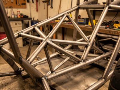 A welded steel sim-racing pedal deck cross-braced to the seat frame with triangulated tube