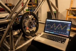 Sim racing cockpit with a laptop showing a brake input curve graph beside the wheel