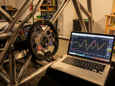 Sim racing cockpit with a laptop showing a brake input curve graph beside the wheel