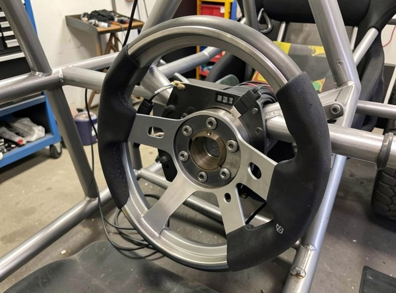 Direct-drive sim racing wheelbase mounted to a welded steel cockpit frame with a quick-release rim