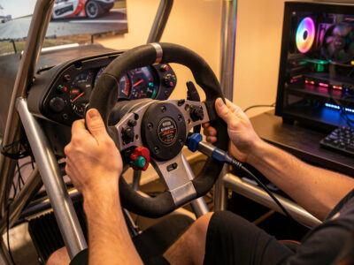 Sim racing wheelbase being unplugged from a console and plugged into a gaming PC mid-swap