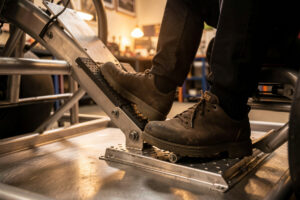 A sim racer's leg pressing a load-cell brake pedal on a welded steel pedal deck