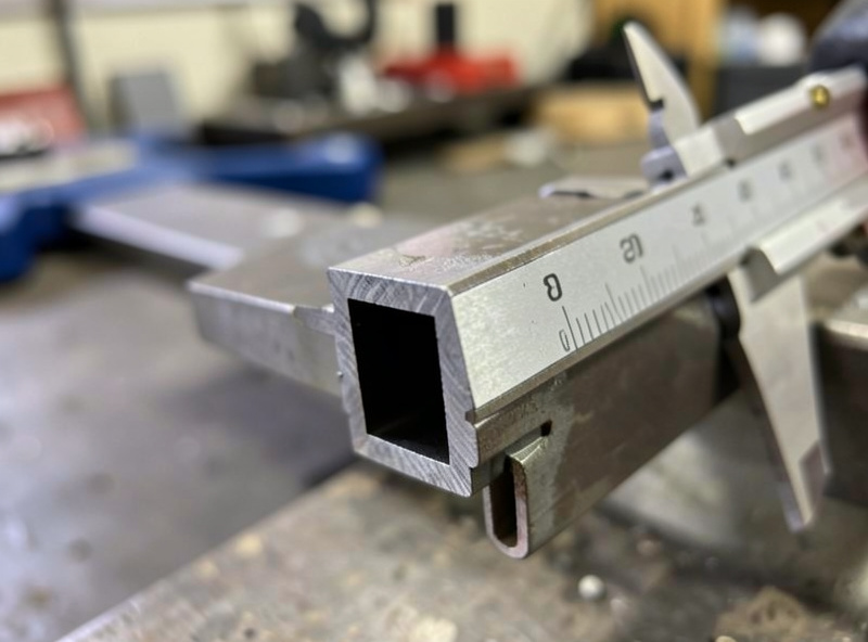 Caliper measuring the wall thickness of a square steel tube cut end