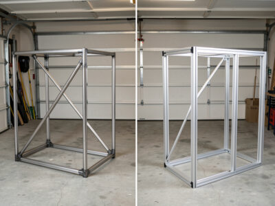 Welded steel-tube sim rig frame beside an 80/20 aluminum extrusion frame in a garage