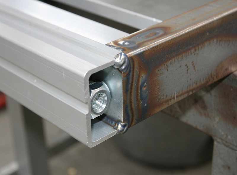 Close-up of an 80/20 aluminum T-slot joint with gusset bracket next to a welded steel corner joint